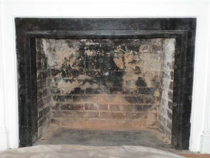 Fireplace with black metal surround and severely damaged firebox before firebox repair