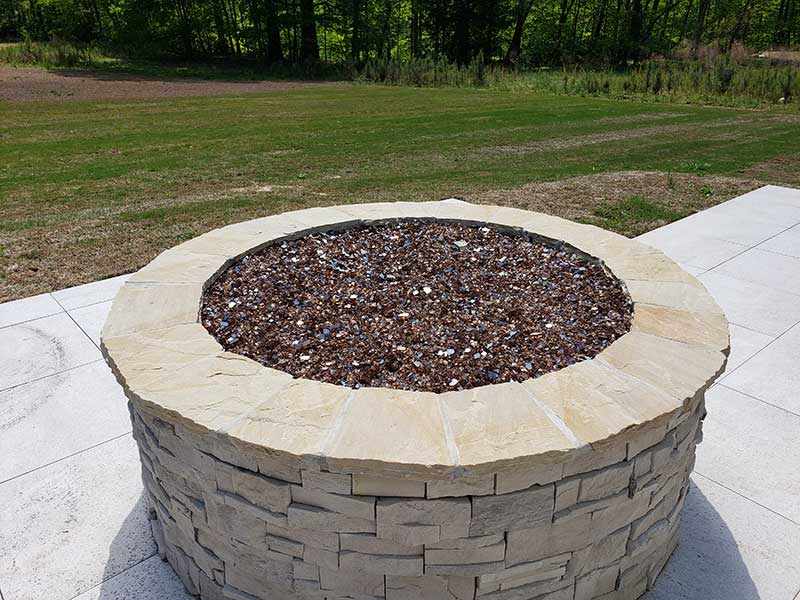Finished custom fire pit made with stacked natural cut stone and decorative fire glass