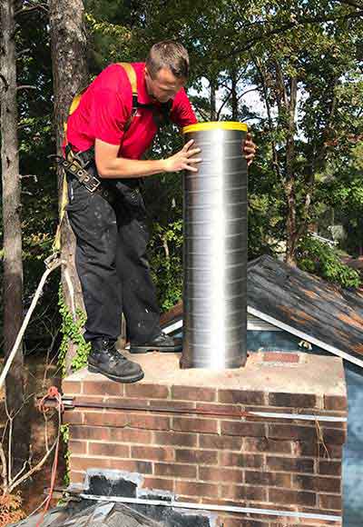 Chimney technician standing on roof fitting new stainless steel chimney lining down through chimney flue