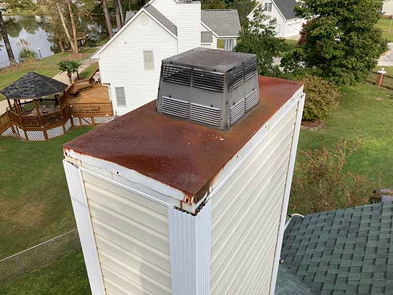 Mr Smokestack Original Photo of Chase Cover Replacement - Before - Broadway and Raleigh, NC Vinyl sided chimney with rusted chase cover and metal chimney cap before chase cover replacement with homes in the background