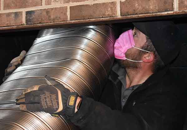 Chimney technician installing a new stainless steel chimney lining through a brick fireplace