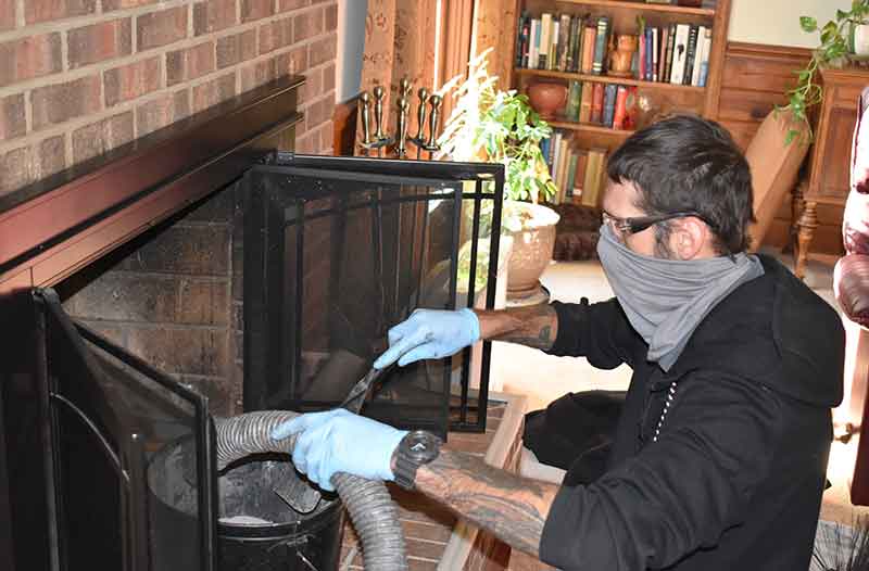 Chimney sweep technician emptying vacuum hose into bucket while performing chimney sweep