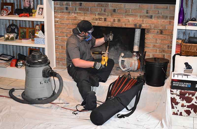 technician working to remove creosote in chimney through fireplace