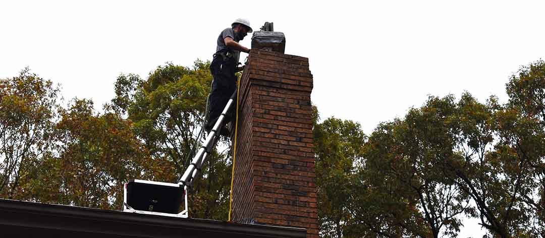 Mr. Smokestack Original Photo of Chimney and Fireplace Inspections - Broadway and Raleigh, NC Chimney technician using specialized chimney inspection equipment while standing on a ladder to reach top of chimney on roof