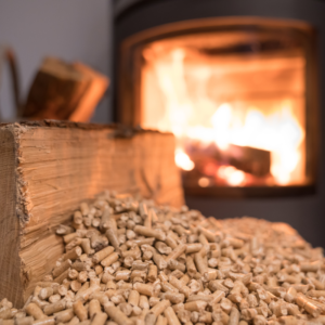 an up-close shot of a piece of wood and some pellets with a lighted stove in the background