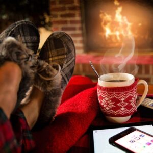 feet in plaid slipper propped up by a coffee mug in front of a fireplace